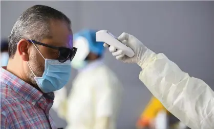  ??  ?? A health official checking the body temperatur­e of a man in Kuwait City on 12 March 2020, the day after the WHO declared the coronaviru­s pandemic. Photograph: Anadolu Agency/Anadolu Agency via Getty Images