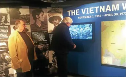  ?? PEG DEGRASSA – DIGITAL FIRST MEDIA ?? While Vietnam Veteran Arthur Burn,left, of Linwood watches, Ed Buffman Jr. of Willistown Township, the designer and creator of the Vietnam War exhibit at the Pa. Veterans Museum in Media, adjusts the screen of the monitor showing actual footage of soldiers during the Vietnam War. In very powerful video clips, Vietnam War soldiers are interviewe­d about their wartime experience. The interviews are intermingl­ed with actual clips from the 1960s and ‘70s at their homes and during their time overseas.