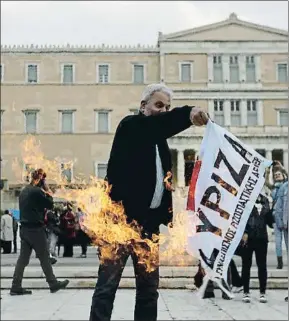  ?? THANASSIS STAVRAKIS / AP ?? Un manifestan­te quema una bandera de Syriza ante el Parlamento