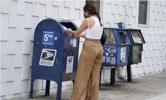  ?? AP FILE ?? TRUSTING THE MAIL: A customer wears a face mask and gloves as she drops mail into a curbside mail collection box in Los Angeles on Monday.