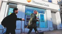  ?? AFP ?? Travellers push suitcases past a closed branch of a Thomas Cook travel agent’s shop in London.