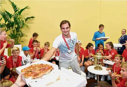  ?? — AFP ?? Have your fill: Switzerlan­d’s Roger Federer offering pizza to ball kids after defeating Argentina’s Juan Martin del Potro in the Swiss Indoors final on Sunday.