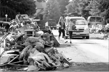  ??  ?? Two women walk down a street piled high with wreckage from floodwater­s as residents clear their homes of damaged property during cleanup in Longmont, Colo., on Thursday. Rescuers continued efforts to reach stranded victims, while electricit­y and phone...