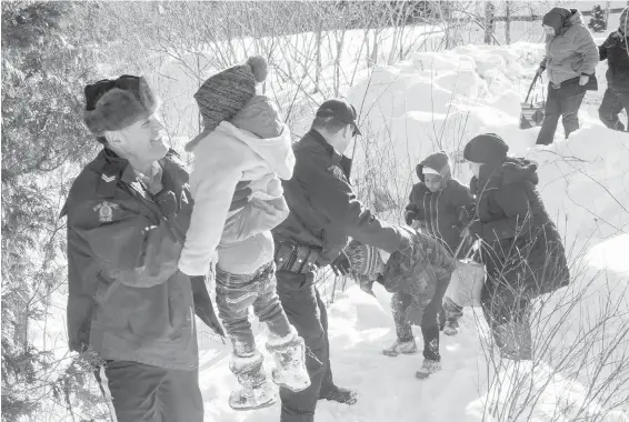  ??  ?? Family members from Somalia are helped into Canada by RCMP officers along the U.S.-Canada border near Hemmingfor­d, Que., on Friday.