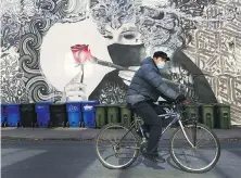  ??  ?? A man wearing a protective mask rides his bicycle past a mask mural in Toronto.