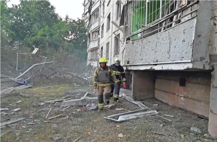  ?? SERGEY BOBOK/AFP VIA GETTY IMAGES ?? Firefighte­rs walk by a partially destroyed building after shelling of multiple rocket launch systems in Kharkiv, Ukraine, on Wednesday.