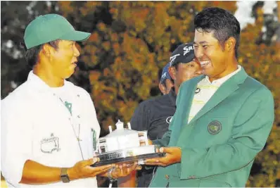  ?? Kevin C. Cox / AFP ?? Matsuyama fa broma amb el seu cadi mentre sosté el trofeu de campió del Masters.