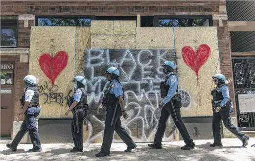  ?? TYLER LARIVIERE/SUN-TIMES FILE ?? Chicago police officers walk by a boarded-up business after a protest on Saturday, June 6.