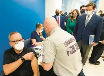  ?? WILFREDO LEE/AP ?? Florida Gov. Ron DeSantis, right rear, watches as Carlos Dennis, 65, rolls up his sleeve so that a Miami-Dade County Fire Rescue paramedic, Capt. Javier Crespo, can administer a COVID-19 vaccine shot at Jackson Memorial Hospital in Miami on Jan. 4, 2021.