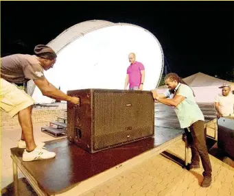  ??  ?? Martin Lewis (second left), CEO of Team Solutions, looks on as Ray Gordon (left) and sound engineer Dwight Bancey (second right) move a speaker into position on the stage at Emancipati­on Park yesterday in preparatio­n for Kanye West’s Sunday Service today. At right with another speaker is Anthony Lawrence.