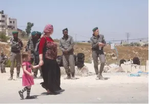  ?? (Marc Israel Sellem/The Jerusalem Post) ?? A WOMAN and her daughter pass by Border Police officers in Beit El yesterday.