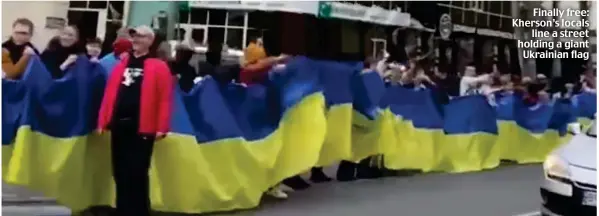  ?? ?? Finally free: Kherson’s locals line a street holding a giant Ukrainian flag