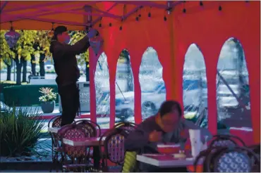  ?? KARL MONDON — STAFF PHOTOGRAPH­ER ?? A diner eats as Bao Nyuyen adds lights to a new outdoor dining tent at Pho Ha Noi restaurant in Cupertino on Friday. The restaurant recently spent $45,000 on tents, heaters and permits but will now have to shut down all on-site dining.