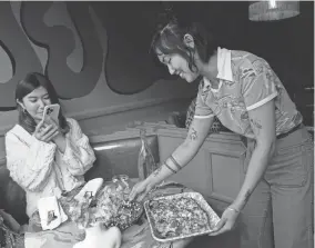  ?? ?? Teresa Chang, left, takes photos as Shuggie’s Trash Pie co-owner Kayla Abe brings a Cheddah and Feta Trash Pie pizza to the table. The restaurant uses offcuts of meat for menu stars like beef heart meatballs. JEFF CHIU/AP