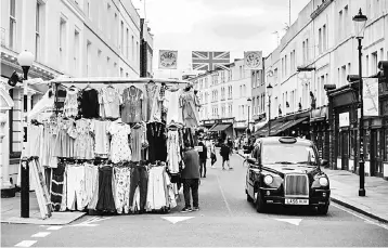  ??  ?? A black London taxi cab drives beneath a Union flag flying over stalls at Portobello Road Market in the Notting Hill district of west London, on August 8. Britain will avoid recession in the coming year but economic growth is expected to lag the euro...