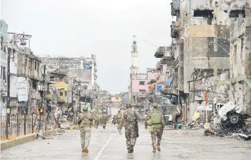  ??  ?? Philippine soldiers walk past destroyed buldings in Bangolo district, after Duterte declared Marawi City ‘liberated’, in Marawi. — AFP photo