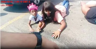  ?? AURORA POLICE DEPARTMENT VIA AP ?? Six-year-old Lovely Gilliam, left, looks up at a police officer as she and her family members lie in a parking lot in 2020 after they were wrongfully forced out of their car in Aurora, Colo.