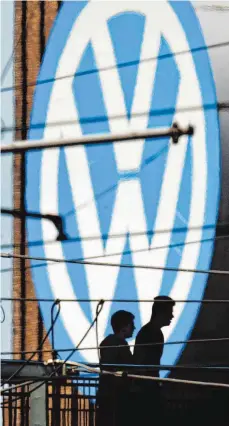  ?? FOTO: DPA ?? Die Silhouette­n von zwei Männern vor dem großen Volkswagen-Logo am VW-Werk: Tricks und Gaunereien in Wolfsburg.