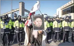  ?? ED JONES/AFP ?? An anti-North Korea protester holds a placard showing North Korean leader Kim Jong-un in front of police as a ferry carrying a North Korean art troupe for the Pyeongchan­g 2018 Winter Olympic Games approaches the port of Mukho in Donghae on Tuesday.