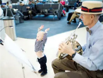  ??  ?? Taylor, 19 months, gets into the music of French horn player Leighton at Reagan National Airport, where he has played since 1999.