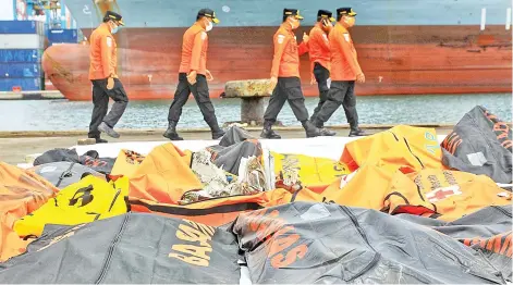  ?? — AFP photo ?? Rescue officials walk past debris collected during the search operation for Sriwijaya Air flight SJ182 at the port in Jakarta.