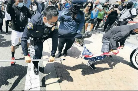  ?? Wally Skalij Los Angeles Times ?? A POLICE OFFICER tries to intervene as a man takes an American f lag from a person at dueling rallies Sunday in Huntington Beach.