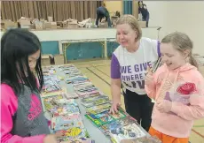  ??  ?? Volunteer Margaret Fiddes, a retired Telus employee, helps Norquay elementary school students Ella Tsang (left) and Tania Bray choose books at the east Vancouver school’s annual book exchange.