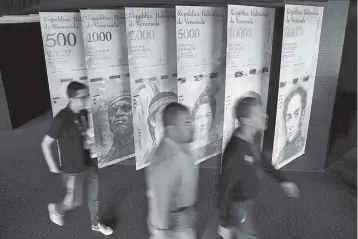  ??  ?? People walk by banners of Venezuelan bolivar notes displayed at the Venezuelan Central Bank building in Caracas,Venezuela. — Reuters photo