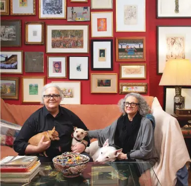  ??  ?? Gina Puzzuoli and Gary Needham relax with their dogs Violet, Dexter and Pete. Behind them on the top row are, from left, an oil by Natalie Hays Hammond (1904-1985), a watercolor by Molly Luce (1896-1986), a collage by Sydney Raynes (1907-1968) and a watercolor by Deborah Rosenthal. Next are, from left, a watercolor by Sonia Delaunay (1885-1979), a photo by Debbie Hill, a watercolor by Diane White and two drawings by Dame Laura Knight (1877-1970). Beneath the White is an oil by Helen Miranda Wilson and beneath the Knights is a Diane White watercolor. On the next row, from left, are a watercolor by Martha Walters, a watercolor by Gwen John (1876-1939) and a watercolor by Edith Dimock (1876-1955). On the next row are, from left, a gouache by Pat Adams, a watercolor by Sarah Mcpherson (1894-1978), a positive etching by an unknown artist, a lithograph by Lesley Dill and an oil by Katherine Freeman. On the bottom row are, from left, a gouache by Doris Lee (1905-1983), a pastel and crayon by Anne Ryan (1889-1954), an oil by Celia Adler (1889-1979) handmade felt and stitching by Adrian Blackstock. Beneath it is a piece by Gary’s mother, Janice Needham. Above the lamp are a watercolor by Ruth Asawa (1926-2013) and a lithograph by Dorothea Tanning (1910-2012).