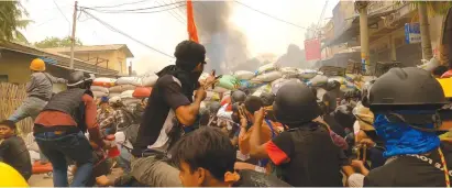  ?? (Reuters) ?? PROTESTERS USE slingshots while taking cover behind a barricade as smoke rises from burning debris during ongoing protests against the military coup yesterday in Monywa, Myanmar.