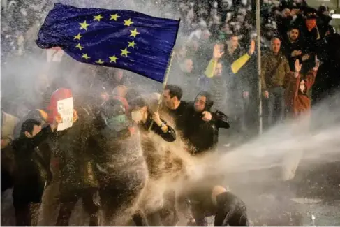  ?? (AFP/Getty) ?? A woman ho l ding a EU f l ag is sprayed by a water cannon in Tbi l isi on Tuesday
