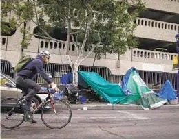  ?? NELVIN C. CEPEDA U-T ?? A bicycle rider passes by several tents in an encampment set up along the sidewalk on E Street in Downtown San Diego on Jan. 31.