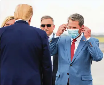  ?? CURTIS COMPTON / CCOMPTON@AJC.COM ?? At the UPS hub at Hartsfield-Jackson Internatio­nal Airport, Gov. Brian Kemp adjusts his mask Wednesday as he greets President Donald Trump on his Georgia visit to tout an infrastruc­ture rule overhaul.