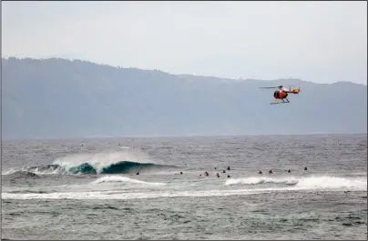  ?? The Associated Press ?? NORTH SHORE: A fire and rescue helicopter flies over a group of surfers on Oahu’s North Shore near Haleiwa, Hawaii, on March 28. Former Hawaii television reporter Angela Keen knows how to track people down. During the coronaviru­s pandemic, she’s putting her people-finding skills to use as one of the original members of a Facebook group that has grown to more than 2,000 people called “Hawaii Quarantine Kapu Breakers.” Kapu is a Hawaiian word that means laws or rules. The group is focused on finding people who violate Hawaii’s 14-day quarantine on travelers arriving to the state.