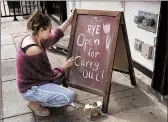  ?? NICHOLAS KAMM/GETTY ?? A woman writes a sign advertisin­g a restaurant serving takeout because of COVID-19 in Washington, D.C.