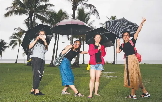  ?? Picture: BRENDAN RADKE ?? RAIN DANCE: Chinese tourists Hui Hui Tao, Yi Shu, Ying Wang and Jiajun Yan brave the elements for a walk on the Esplanade.