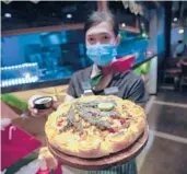  ?? SAKCHAI LALIT/AP ?? A staff member holds a pizza with a cannabis leaf last week at a restaurant in Bangkok, Thailand. The Pizza Company has been promoting its “Crazy Happy Pizza.”