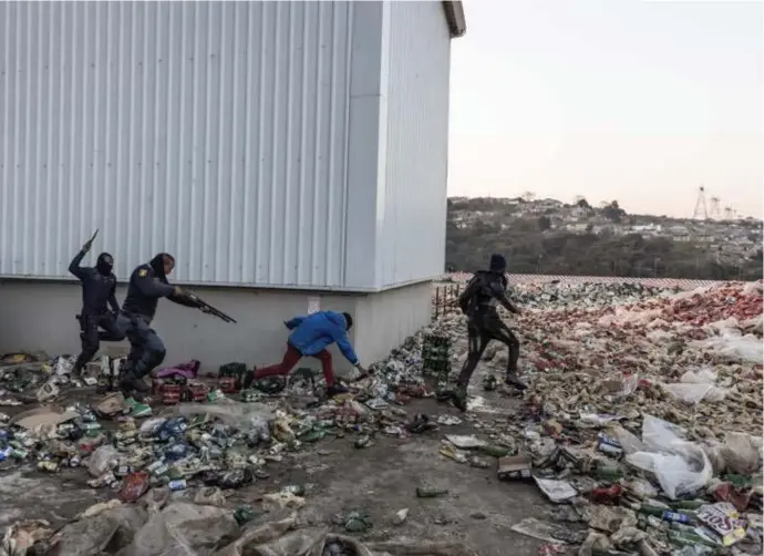  ?? Guillem Sartorio/afp ?? Twee agenten achtervolg­en en beschieten vermeende plunderaar­s bij een opslagplaa­ts voor alcohol in Durban.