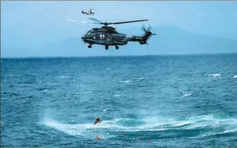  ?? XINHUA ?? A helicopter lowers a harness into the water during the rescue of 12 sailors in waters off Huidong, Guangdong province, on Sunday morning. The seamen went into the water when their ship, which had been carrying sand, capsized. The cargo shifted after a...