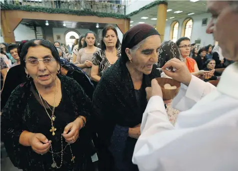  ?? SAFIN HAMED/Getty Images ?? Iraqi Christians receive communion during a mass at the Saint-Joseph church in Irbil, the capital of the autonomous Kurdish region of northern Iraq. Hun
dreds of Christian families fled their homes in Mosul after the jihadist Islamic state told them...