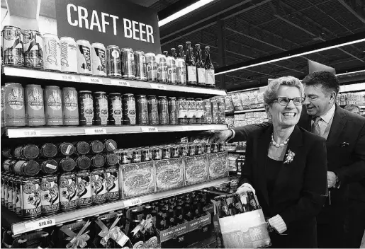  ?? NATHAN DENETTE / THE CANADIAN PRESS ?? Ontario Premier Kathleen Wynne, left, and Minister of Finance Charles Sousa pick up beer at a Loblaws grocery store in Toronto Tuesday. The Liberals aim to have six-packs available at 58 Ontario grocery stores by the end of December.