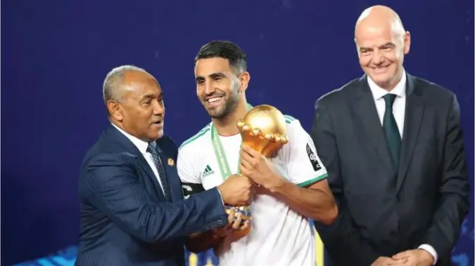  ?? FOTO: SUHAIB SALEM/REUTERS, NTB SCANPIX ?? KORRUPSJON­SMISTANKER: Kaptein Riyad Mahrez får beviset på at Algerie vant fjorårets Afrikamest­erskapet i fotball fra Ahmad Ahmad, visepresid­ent i Fifa. Fifa-president Gianni Infantino følger med. Nå er den afrikanske visepresid­enten i Fifa i trøbbel.