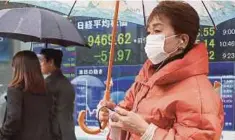  ?? [ FOTO AP ] ?? Seorang wanita melintasi papan saham elektronik firma sekuriti di Tokyo, semalam.