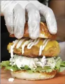  ??  ?? A handler tops a Krispy Fried Chk’n sandwich with a doughy pretzel bun .