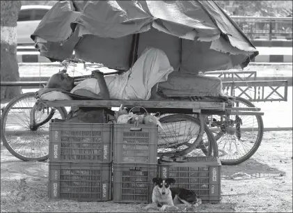  ?? Associated Press ?? An Indian man rests on a hand cart under a market umbrella during the heat Thursday in Ahmadabad, India. Eating onions, lying in the shade and splashing into rivers, Indians were doing whatever they could to stay cool during a brutal heat wave that has...