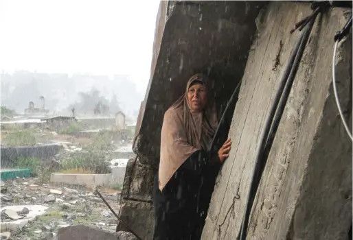  ?? — REUTERS ?? A woman shelters from the rain as Palestinia­ns visit the graves of people who were killed in the ongoing conflict between Israel and Hamas on Eid Al Fitr in Gaza Strip on Wednesday.