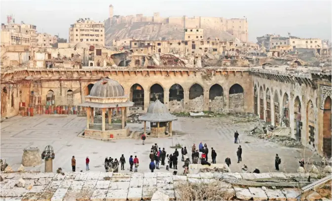  ?? — AP ?? ALEPPO: In this Thursday, Jan 19, 2017 photo, people visit the courtyard of the heavily damaged Great Mosque of Aleppo, overshadow­ed by a 13th century citadel, in the Old City of Aleppo.