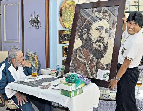  ??  ?? Fidel Castro, celebratin­g his 89th birthday with a glass of beer, is presented with a portrait of himself as a young man by Evo Morales, the president of Bolivia