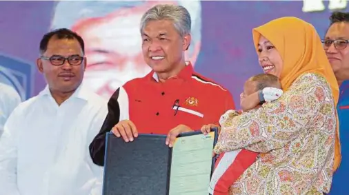  ?? PIC BY RASUL AZLI SAMAD ?? Deputy Prime Minister Datuk Seri Dr Ahmad Zahid Hamidi handing over a birth certificat­e to a woman and her child at the Home Ministry Open Day in Ayer Keroh yesterday. With him are his deputy, Datuk Nur Jazlan Mohamed (right), and Chief Minister Datuk...