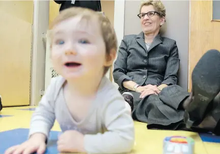  ?? ELLIOT FERGUSON / POSTMEDIA NEWS FILES ?? Ontario Premier Kathleen Wynne sits with a baby at a child care centre in Kingston. The Liberal government is proposing a $930-million plan to give ‘free’ daycare to every Ontarian child.